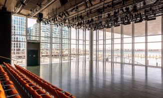 Photo of theatre with orange rows of seats and large glass windows overlooking Boston harbor