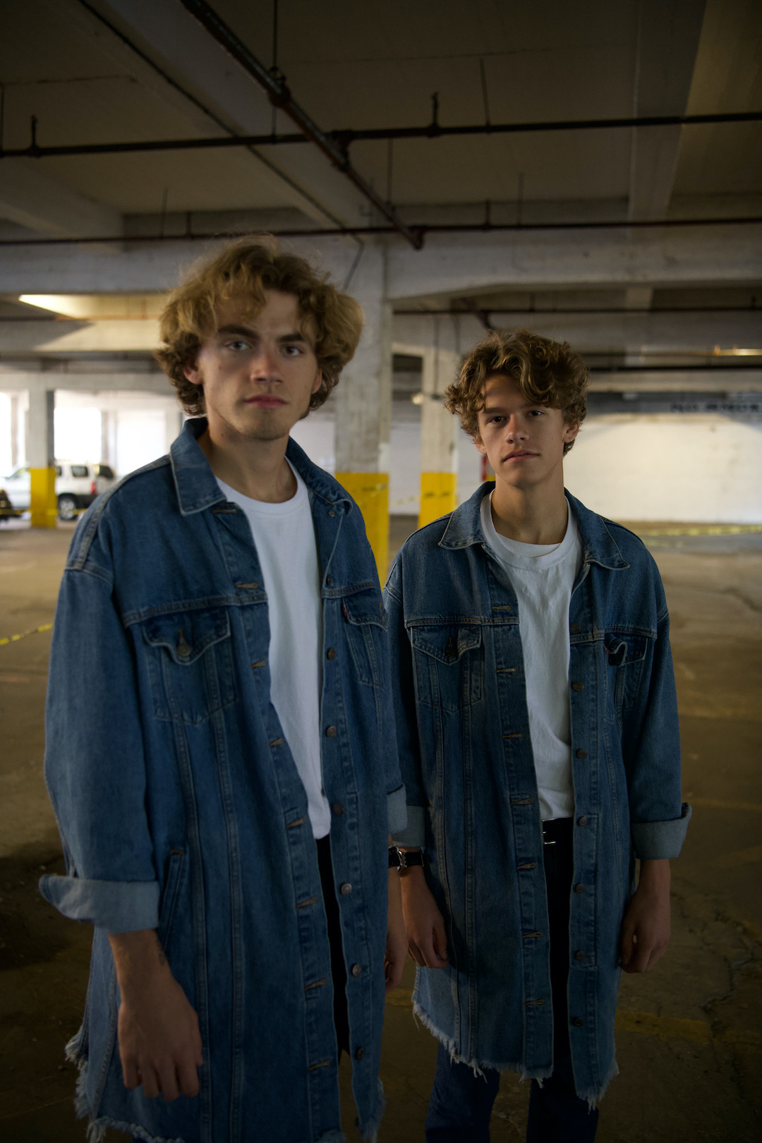Two light-skinned blonde men in denim shirts standing in parking garage.