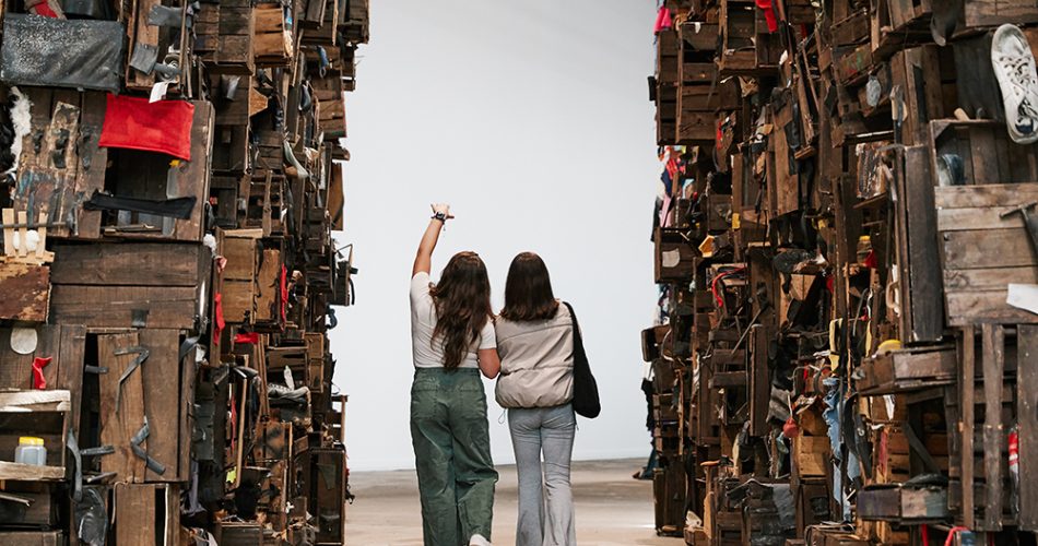 Two people walking between large walls covered in crates