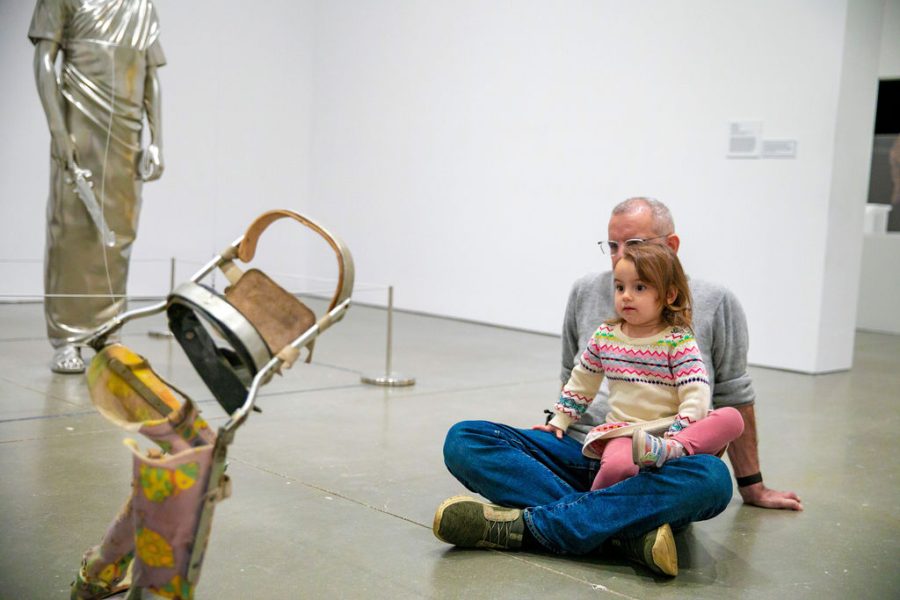 A child sits in her parent's lap on the floor of a gallery, looking at artwork