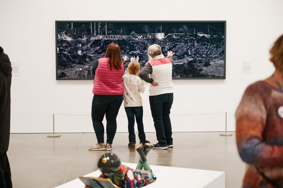 A child and two adults look at a horizontally oriented artwork