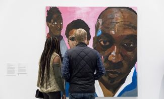 Visitors looking at painting of a Black man's face in foreground with 2 figures over his shoulder