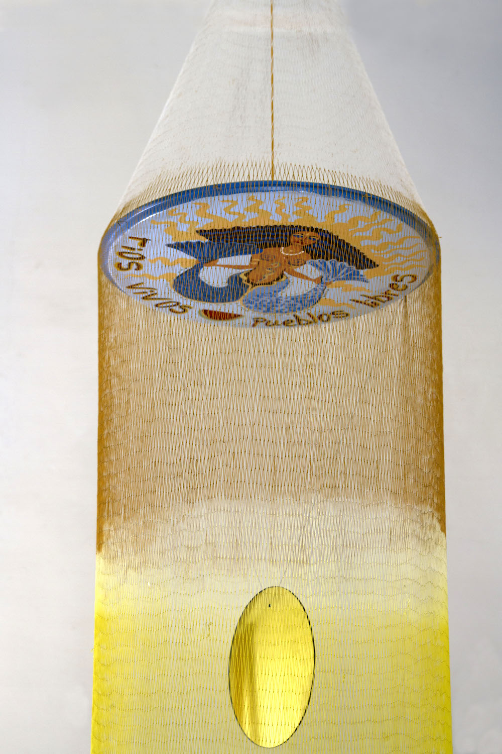 A form that looks like a mobile or a fishing net with orange and yellow fibers hangs suspended. At the bottom, small objects hang from strings in a corkscrew shape.