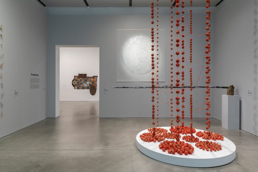 Gallery with circular white drawing on wall and red stringed installation hanging from ceiling