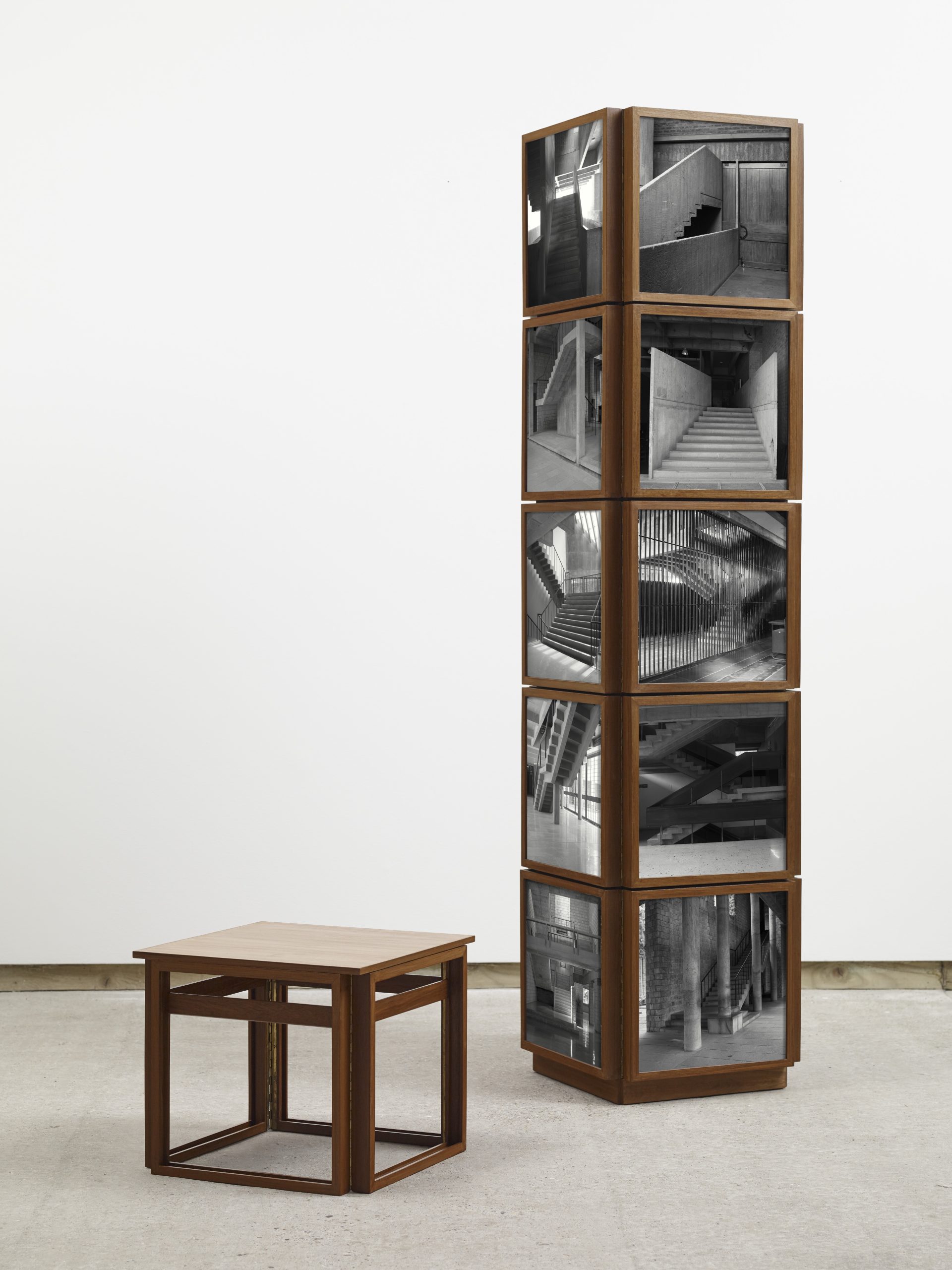 Wooden pillar covered with black and white photos of staircases and accompanying stool