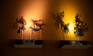 Paper shadow puppets lit against orange wall