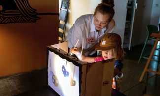 A child and adult holding up shadow puppet in a lit box
