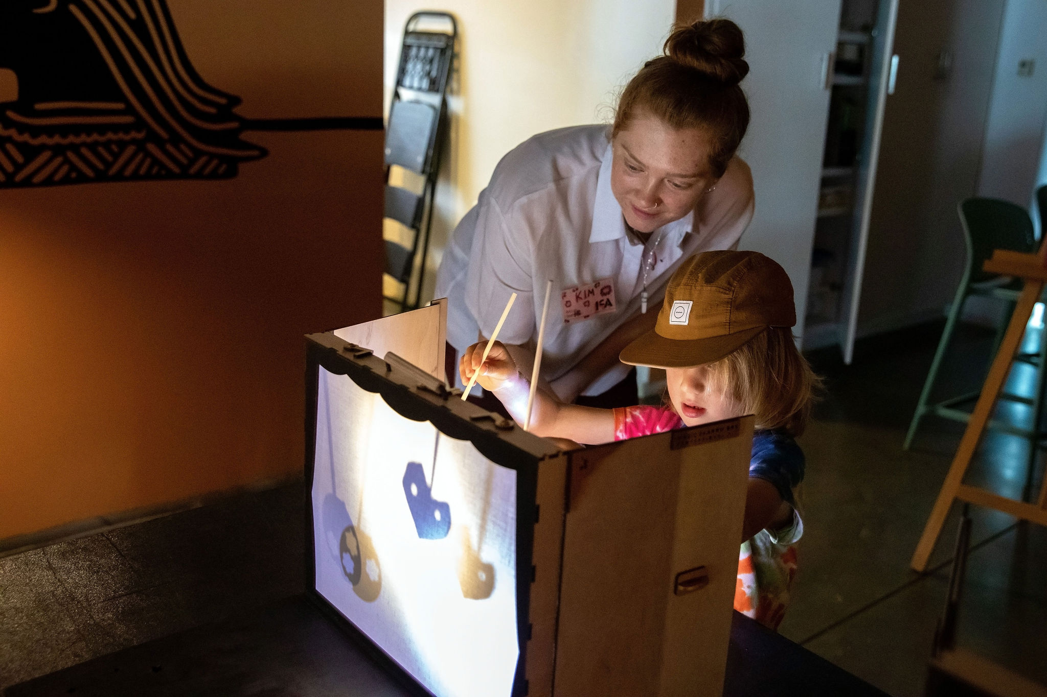 A child and adult holding up shadow puppet in a lit box