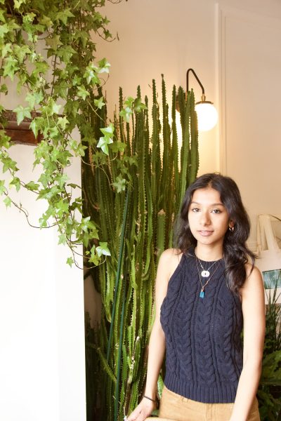 Person with long dark hair and a blue crop top seated in front of indoor plants