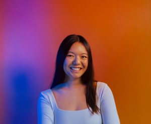 Headshot of a woman with long black hair smiling against a colorful gradient background