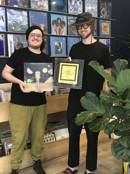 two men hold up vinyls while smiling.