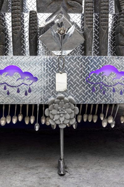 Close up of the front of a metal bus with a flower figure at the front and rainclouds on either side of the flower