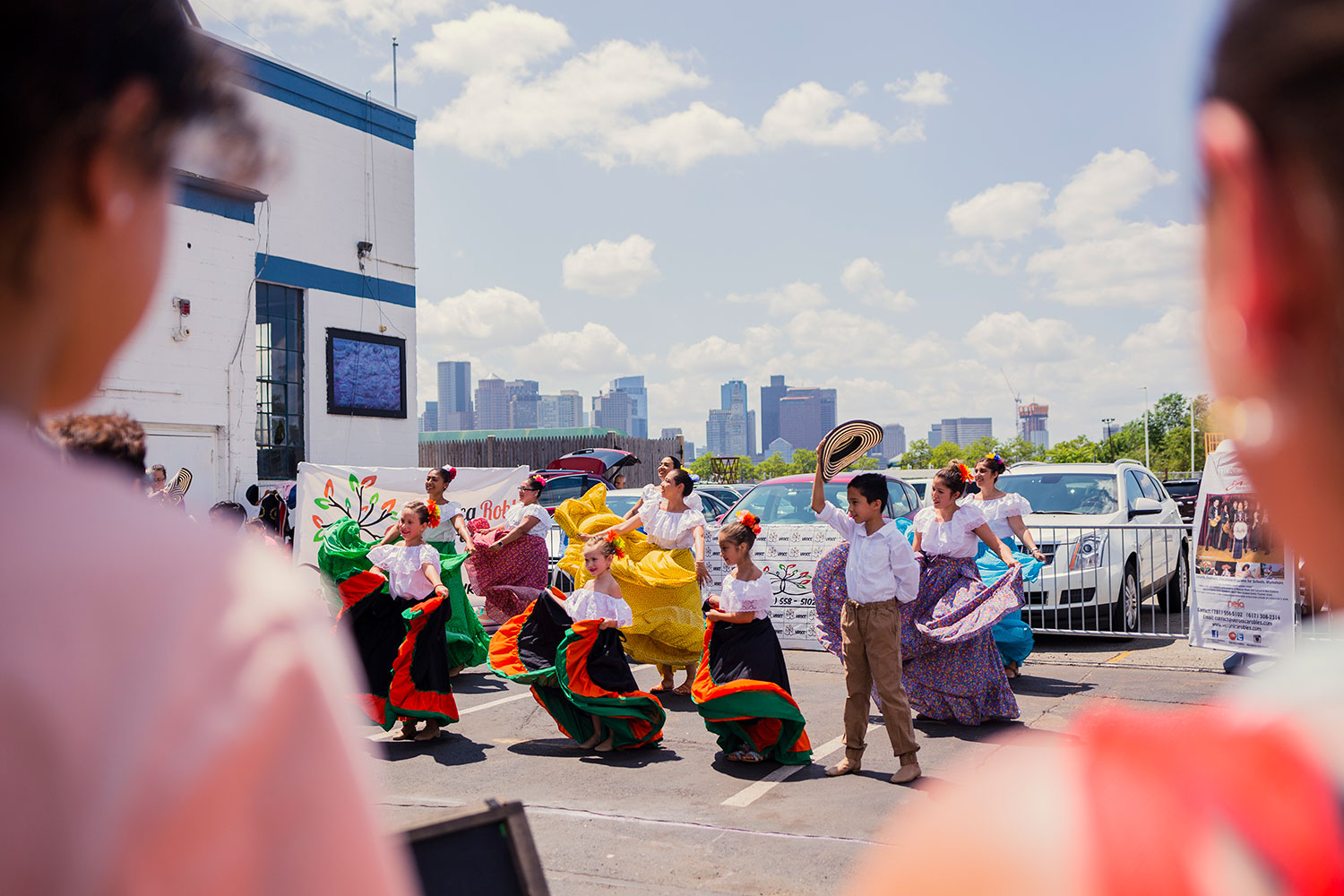 Children in traditional folklorico outfits dancing in a parking lot