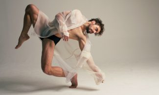 Man in see-through robe in a dance pose on one foot