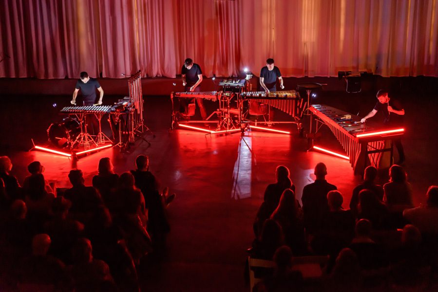 Four people playing mallet percussion instruments with red neon on them.