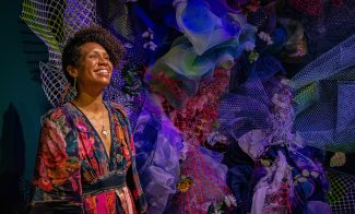 Person with medium-toned skin smiling in front of dark jewel colored mesh and fabric installation