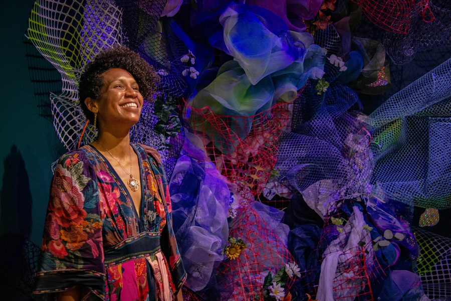 Person with medium-toned skin smiling in front of dark jewel colored mesh and fabric installation