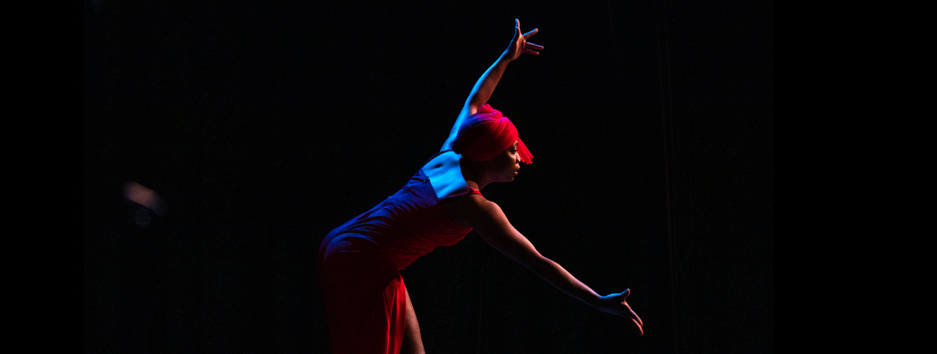Dancer in red and blue outfit lit in low lighting