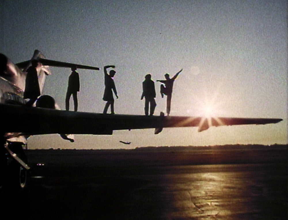 Five people stand on the wing of an airplane with a sunset in the background