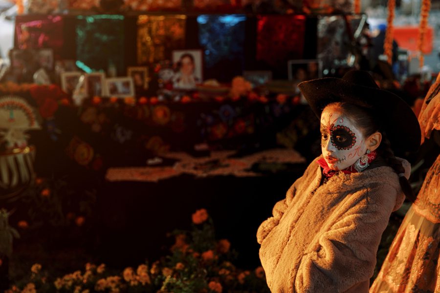 Child with skull face paint in front of Day of the Dead altars