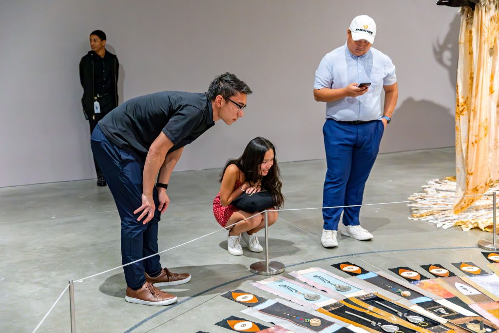 Three people crouch down to look at Tau Lewis' circular artwork