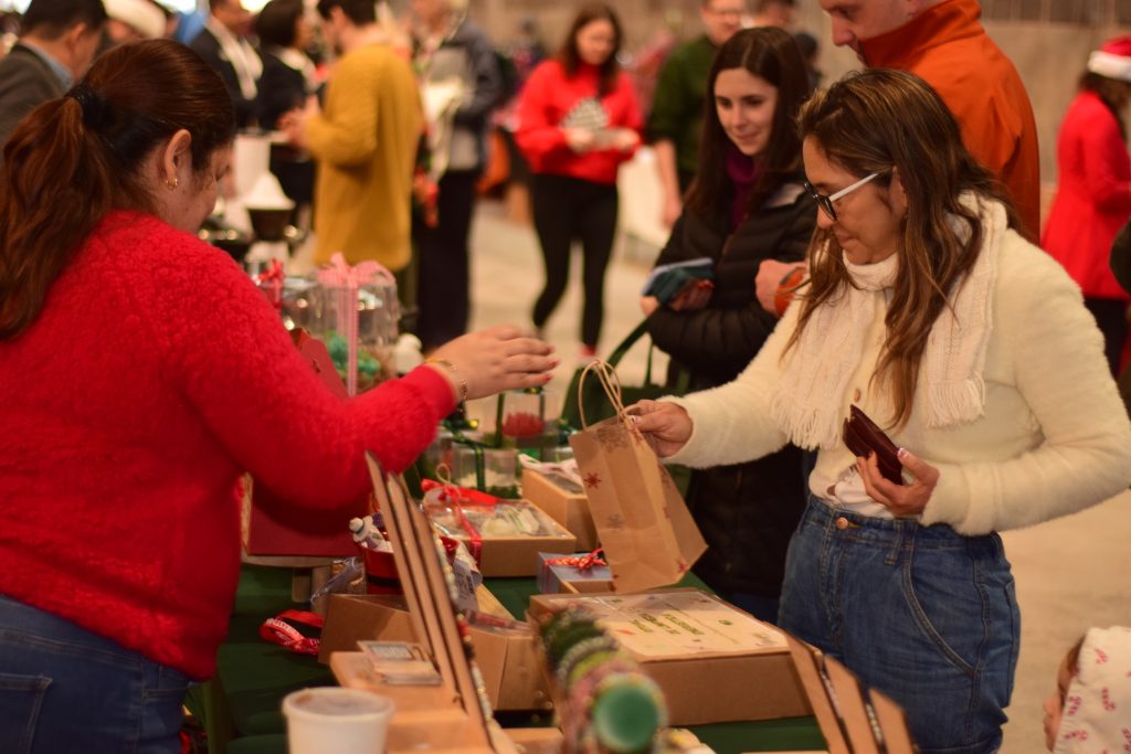 Shoppers in winter clothes in front of a table at an indoor market