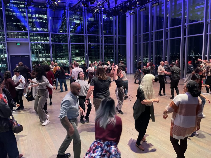 Many people dancing in a large room with glass walls