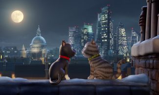 Two animated cats wearing a red collar and a green collar sit on a snowy rooftop at night, gazing at each other. A full moon and city skyline with tall buildings in the background create a romantic scene.