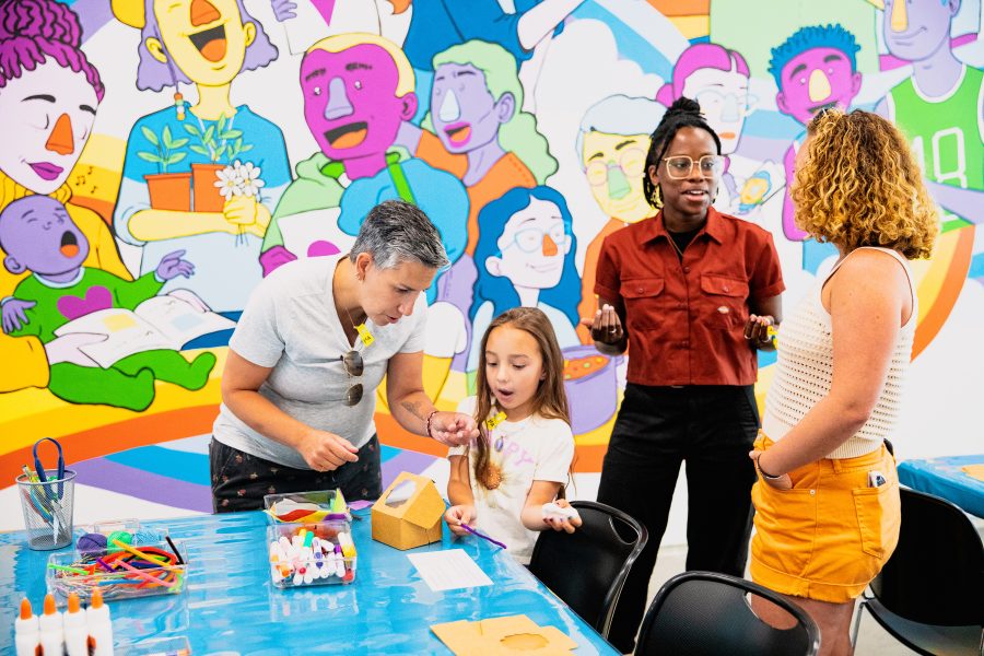 Four people stand and make crafts in front of a mural