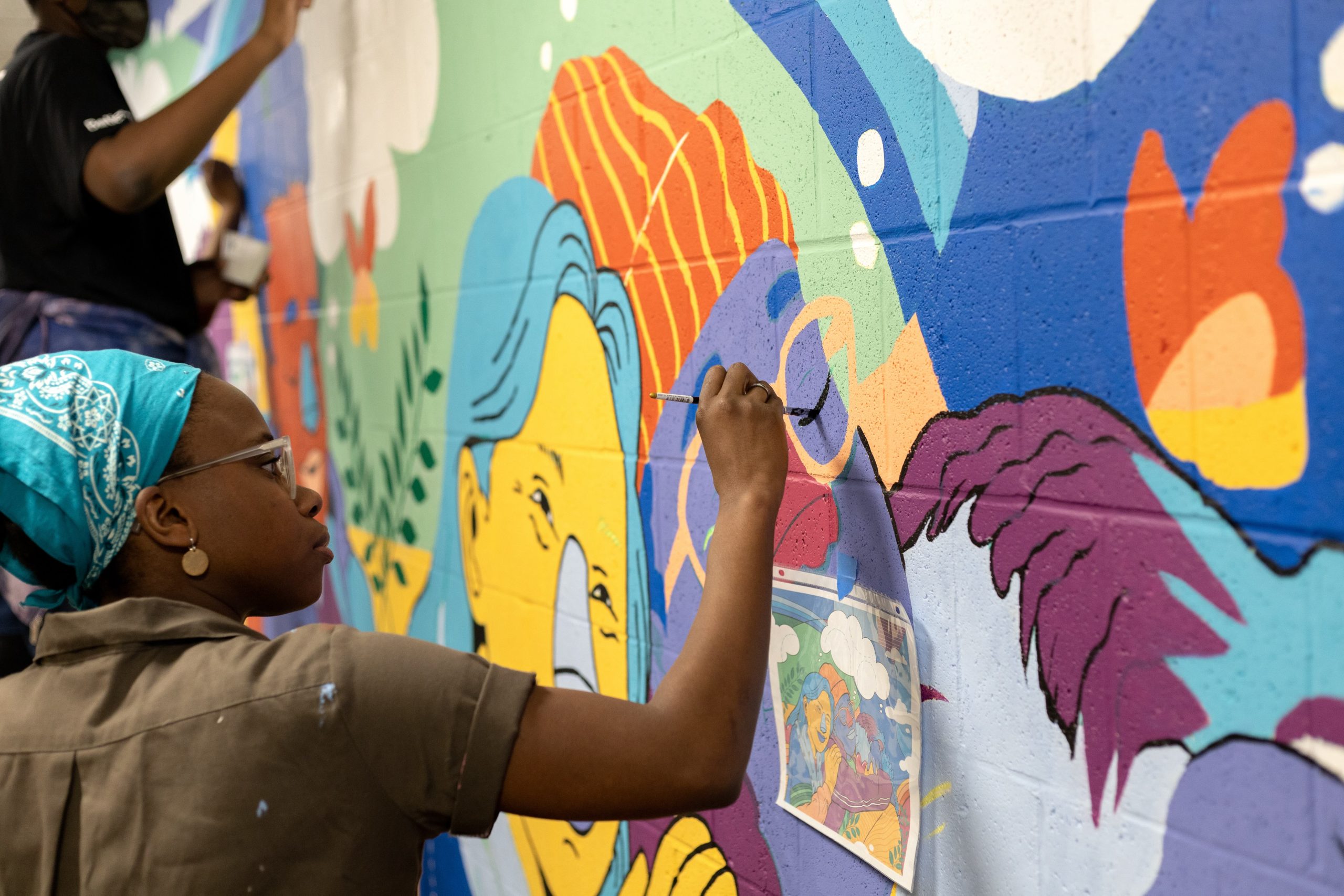 a person in a green shirt and blue bandana paints on a colorful brick wall