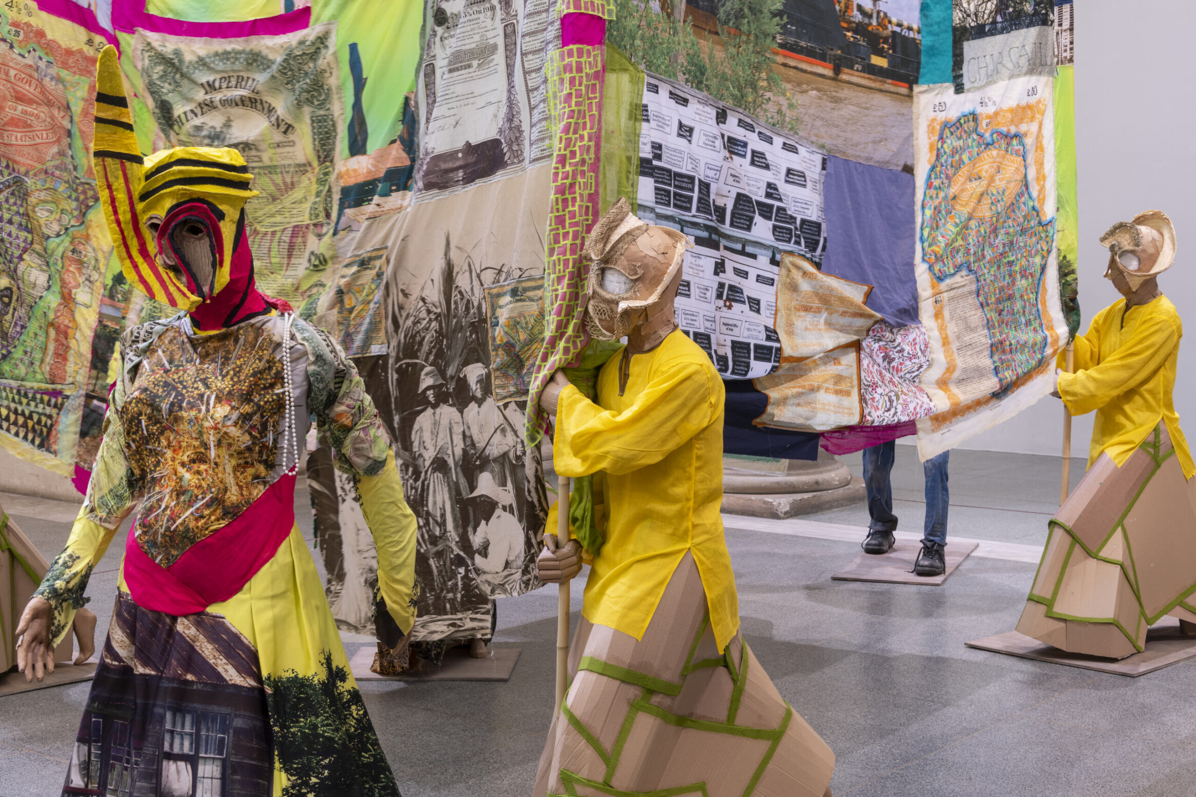 installation view of figures adorned in colorful fabric carrying flags