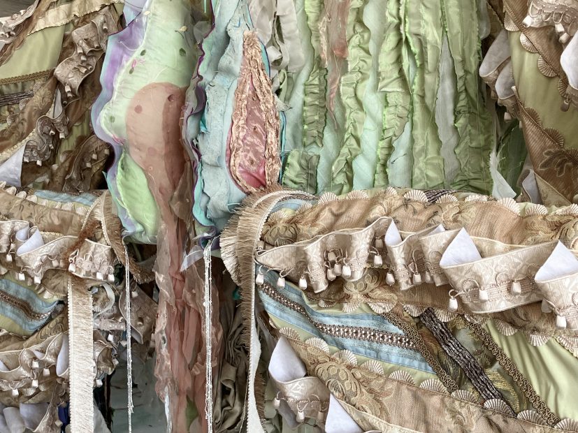 An artwork made of assorted fabrics and ornamentations in pale pastel shades.