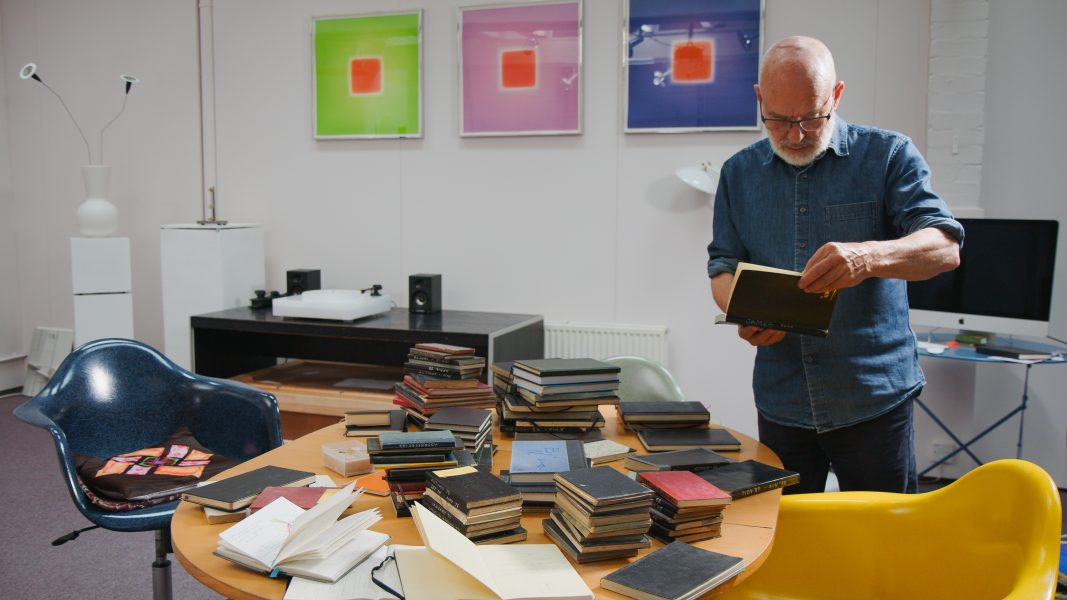 Brian Eno looking at book surrounded by studio space