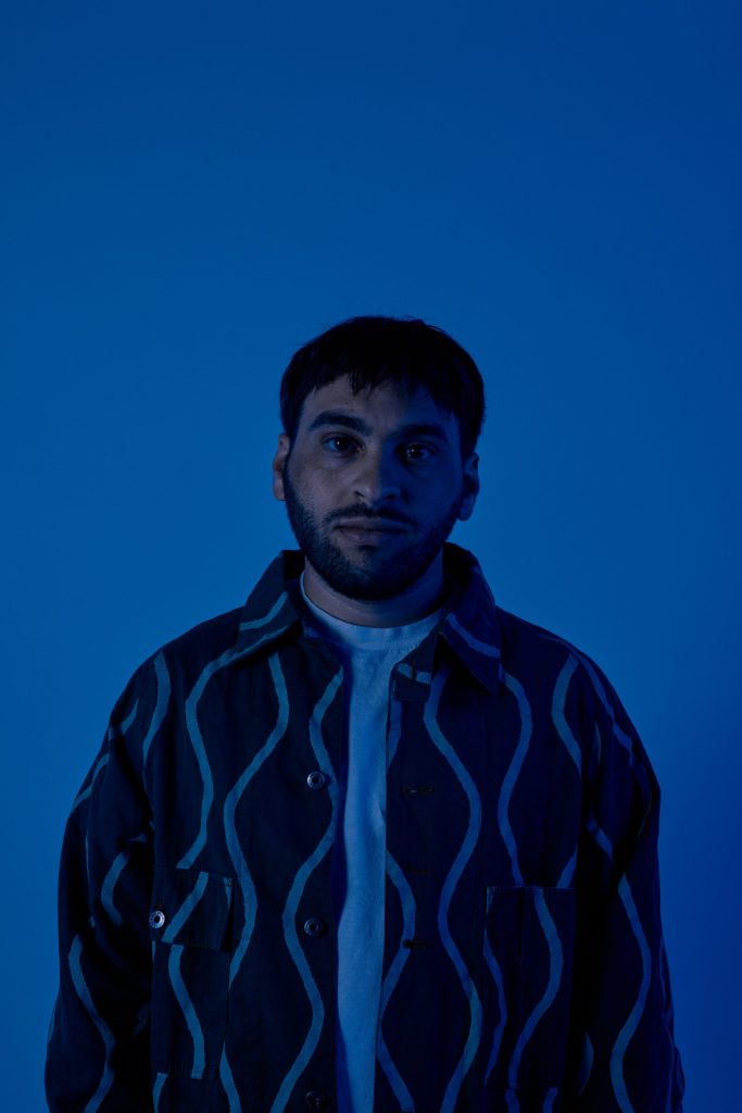 Photo of person with short hair and a beard in dark blue lighting