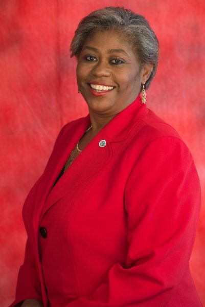 Headshot of person with dark skin and red coat against red background