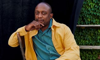 Artist Hank Willis Thomas in bright yellow and blue collared shirts sitting outside on a bench