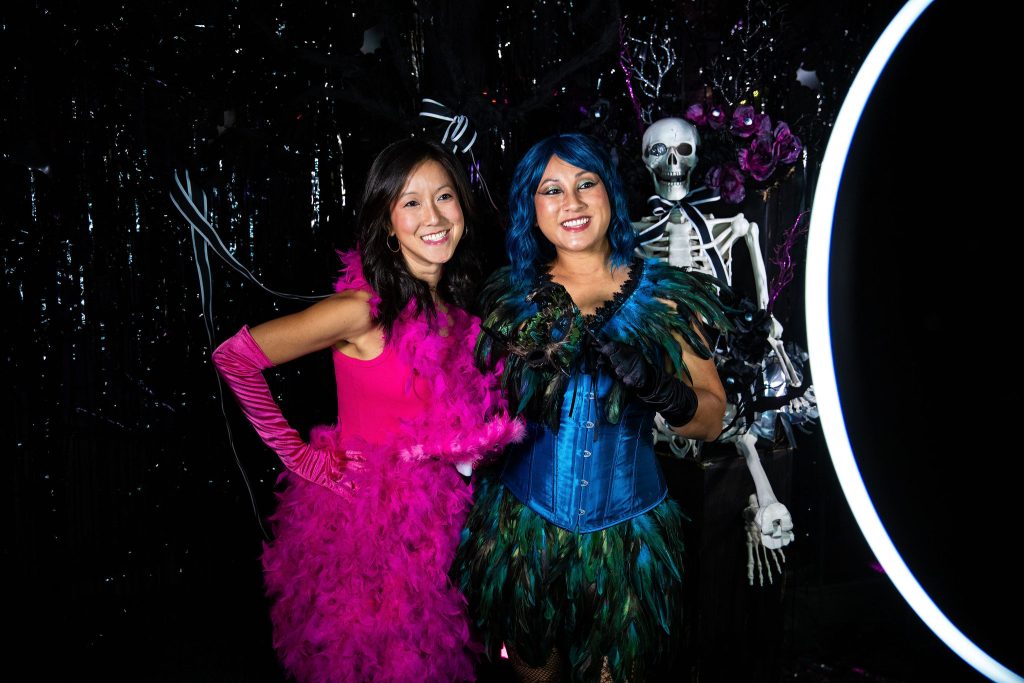 Two people in brightly colored costumes pose for a photo with a skeleton