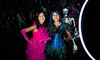 Two people in brightly colored costumes pose for a photo with a skeleton