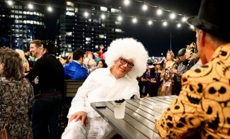 Person in white outfit and white wig sitting at an outdoor Halloween party