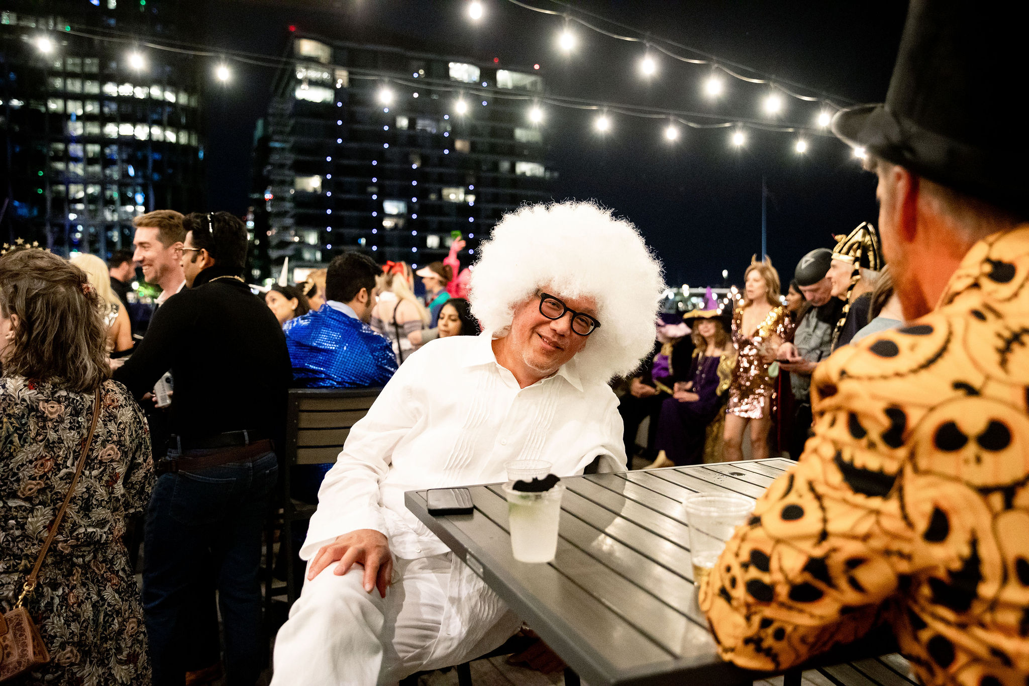 Person in white outfit and white wig sitting at an outdoor Halloween party