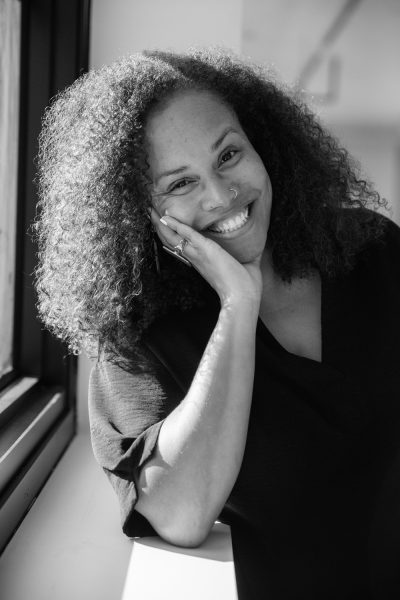 Black and white headshot of person with long curly hair sitting by a window