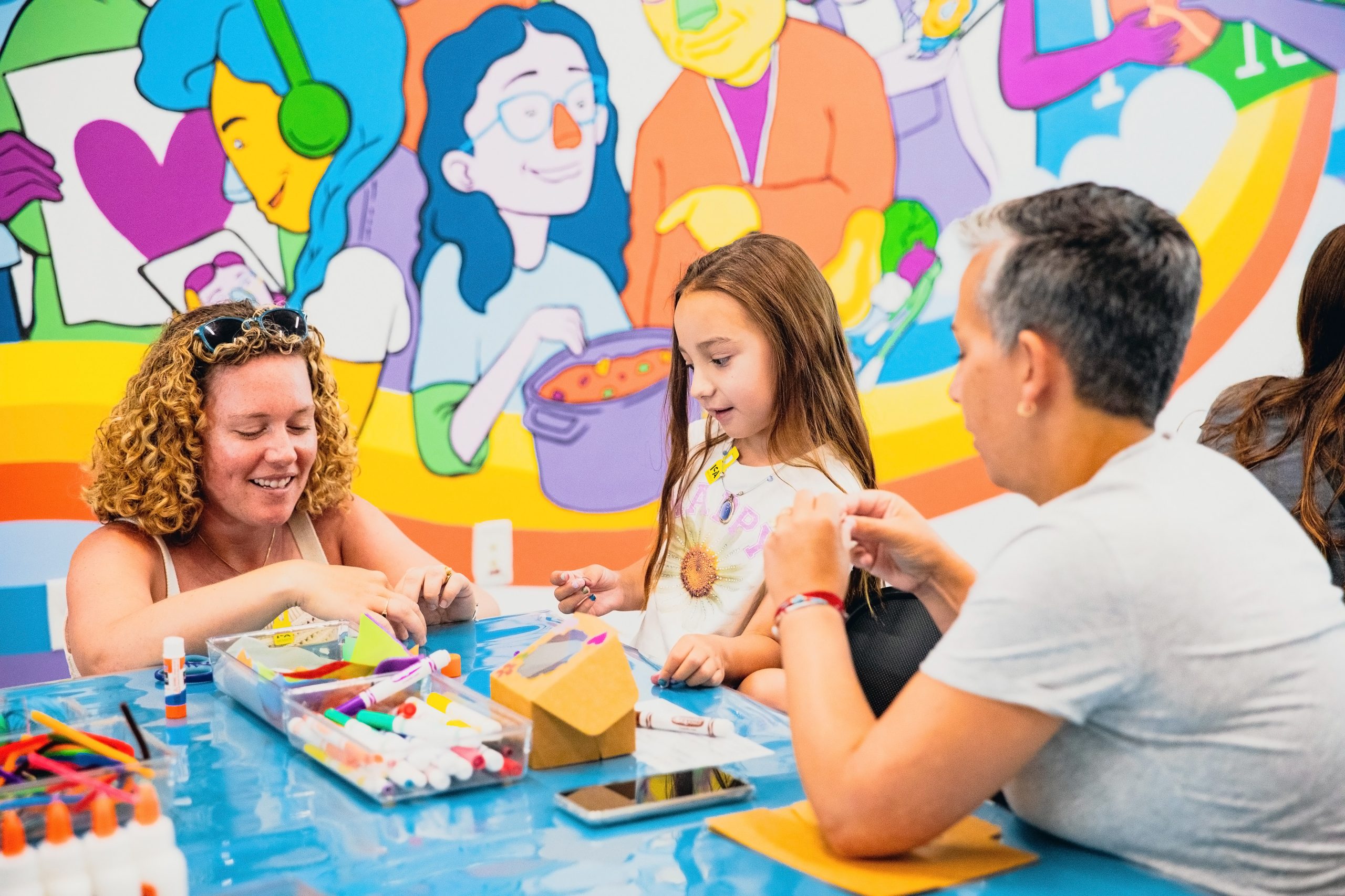 A small child makes art with 2 parents in front of a colorful painted mural