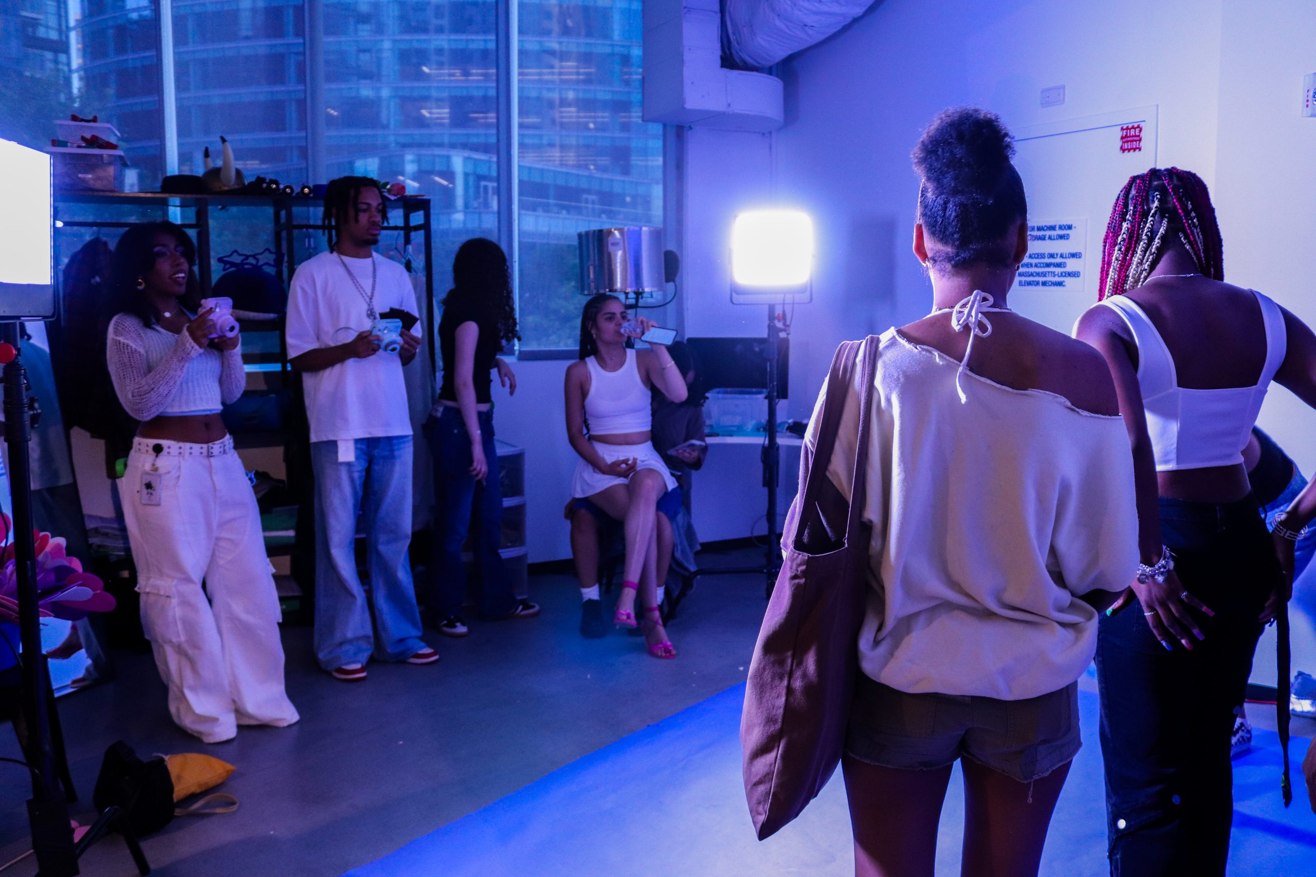 Four teens near one wall and two large lights on stands greet two teens walking into Seaport Studio's photo booth and get ready to take their photo