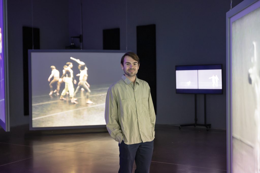 Curatorial Assistant Max Gruber in a dark gallery with various-sized video screens displaying dancers