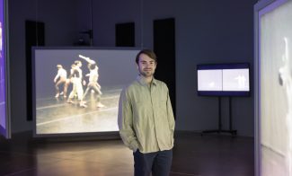 Curatorial Assistant Max Gruber in a dark gallery with various-sized video screens displaying dancers