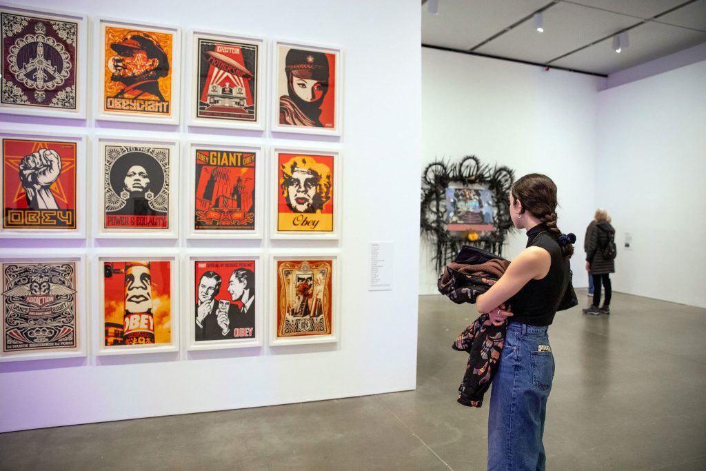 A visitor looking at a wall of Shepard Fairey graphic prints