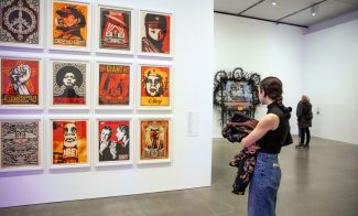 A visitor looking at a wall of Shepard Fairey graphic prints