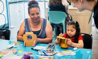 A parent and a child decorate small cardboard boxes together