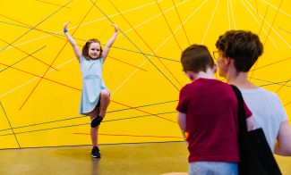 A parent watching a child hold a dance pose against a yellow wall