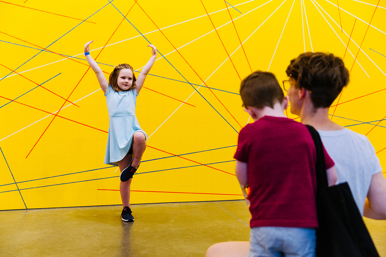 A parent watching a child hold a dance pose against a yellow wall